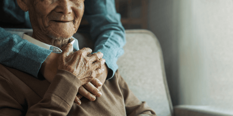 A person embracing their older family member sitting in a chair