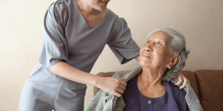 A caregiver placing a sweater on a senior woman’s shoulders in her home