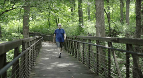 Elderly man walking on a wooden bridge in a forest.